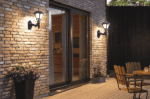 Wall side lanterns illuminating an outdoor patio with brick wall and wooden furniture.